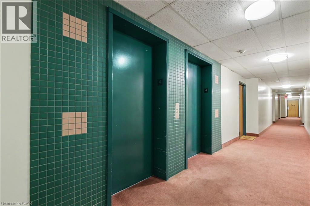Hallway featuring two elevators with green tile surrounds, flush-mounted lighting, white walls, and pink carpeting - 175 Hunter Street E Unit# 401, Hamilton, ON - Indoor Photo Showing Other Room