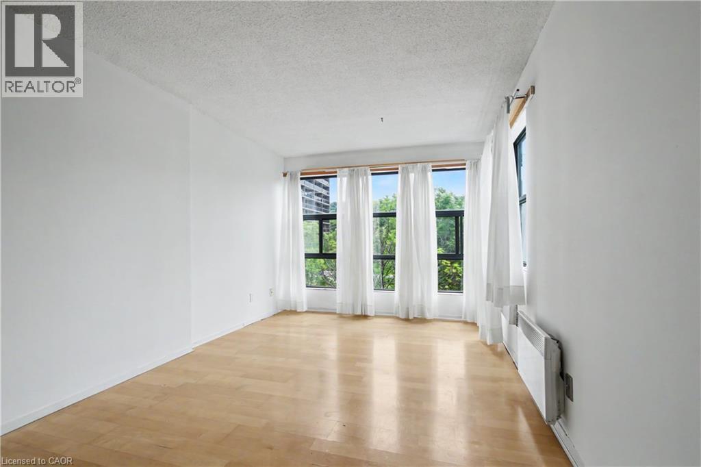 Bright room featuring light wood-finish flooring, white walls, and multiple windows with white drapery - 175 Hunter Street E Unit# 401, Hamilton, ON - Indoor Photo Showing Other Room