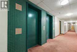 Hallway featuring two elevators with green tile surrounds, flush-mounted lighting, white walls, and pink carpeting -