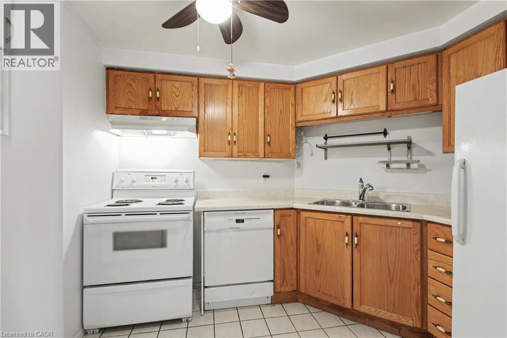 Kitchen featuring wood-finish cabinetry and white appliances, including a range, dishwasher, and refrigerator - 175 Hunter Street E Unit# 401, Hamilton, ON - Indoor Photo Showing Kitchen With Double Sink