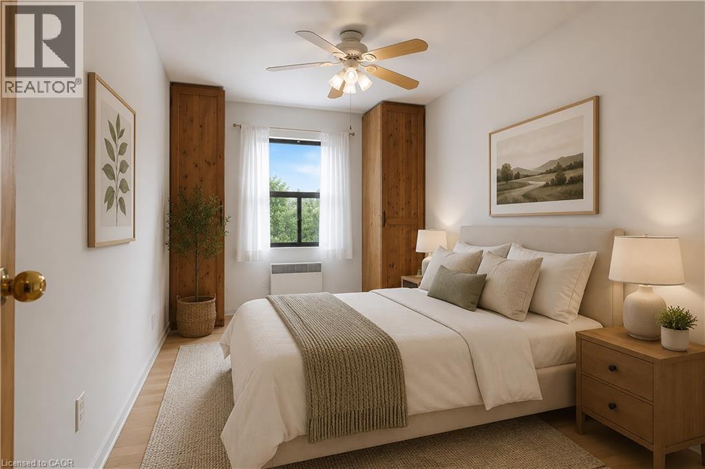 Bright room featuring wood-finish flooring, a ceiling fan with light fixture, and a window with white sheer curtains - 175 Hunter Street E Unit# 401, Hamilton, ON - Indoor Photo Showing Bedroom