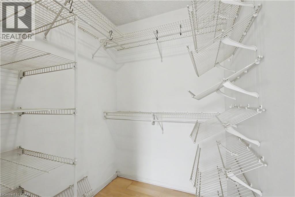 Walk-in closet featuring white wire shelving, multiple hanging rods, and light wood-finish flooring - 175 Hunter Street E Unit# 401, Hamilton, ON - Indoor With Storage