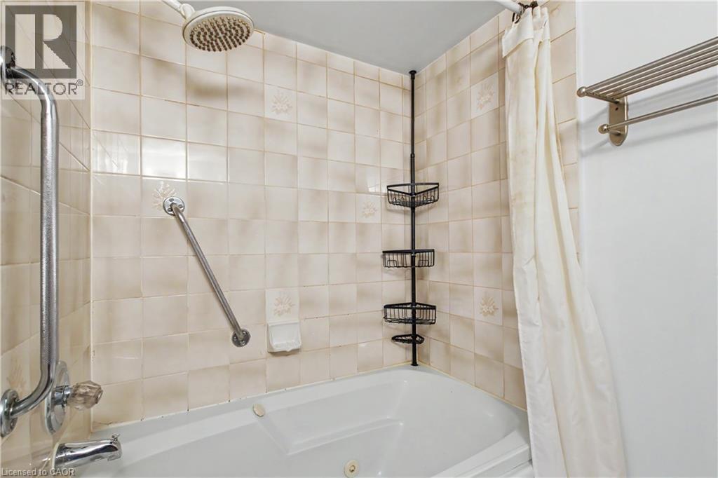 Tiled shower surround with a corner tub featuring a shower head and grab bars - 175 Hunter Street E Unit# 401, Hamilton, ON - Indoor Photo Showing Bathroom
