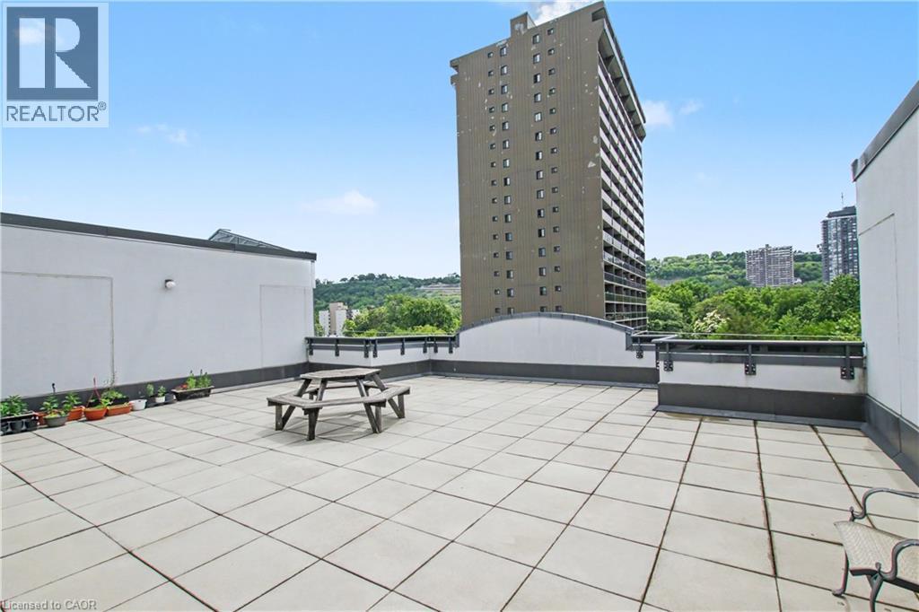 Spacious rooftop patio featuring large format tile flooring and a perimeter wall with dark railings - 175 Hunter Street E Unit# 401, Hamilton, ON - Outdoor
