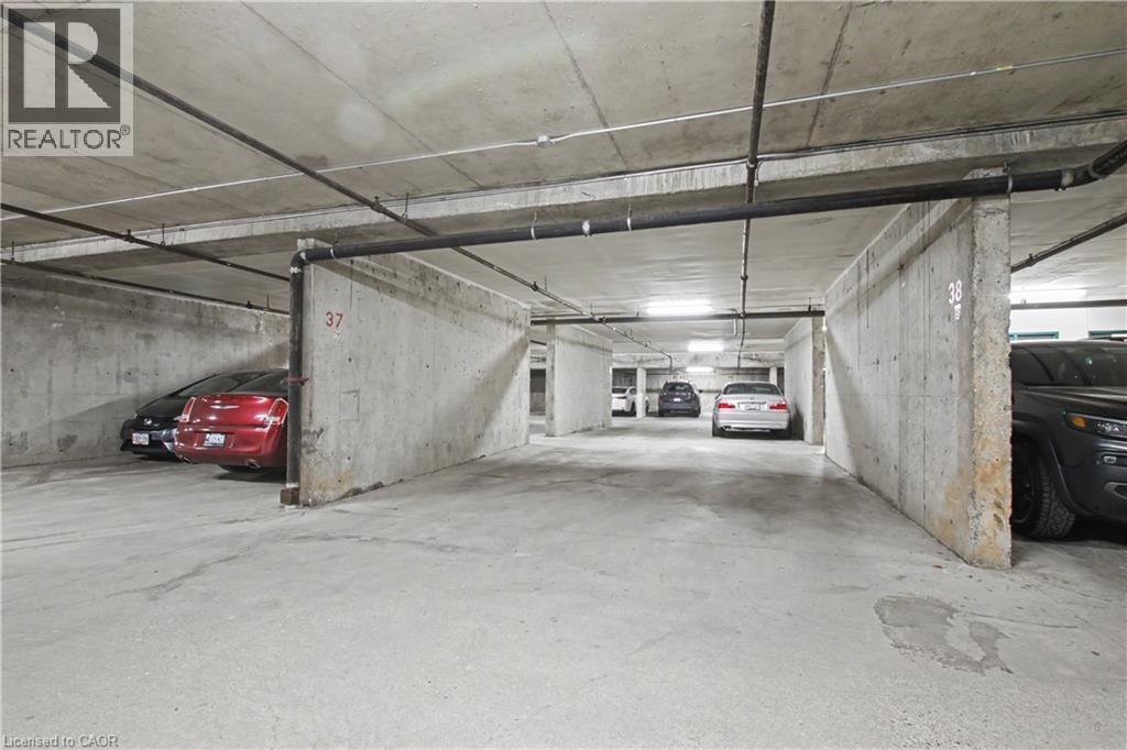 Underground parking garage featuring concrete walls, concrete flooring, exposed overhead piping, and overhead lighting - 175 Hunter Street E Unit# 401, Hamilton, ON - Indoor Photo Showing Garage