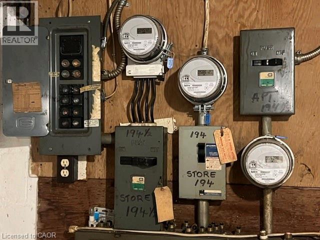 Electrical service panel system with multiple meters and circuit breaker boxes mounted on a wood-paneled wall - 194 Kenilworth Avenue N, Hamilton, ON