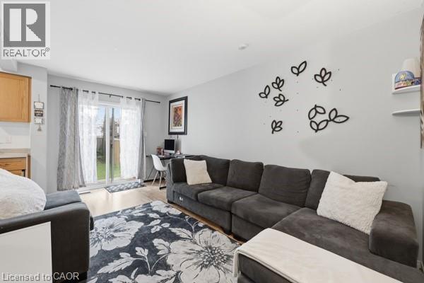 Light wood-finish flooring complements the neutral wall color in this versatile living area, featuring a sliding glass door providing direct outdoor access - 16 Harrison Avenue, Hamilton, ON