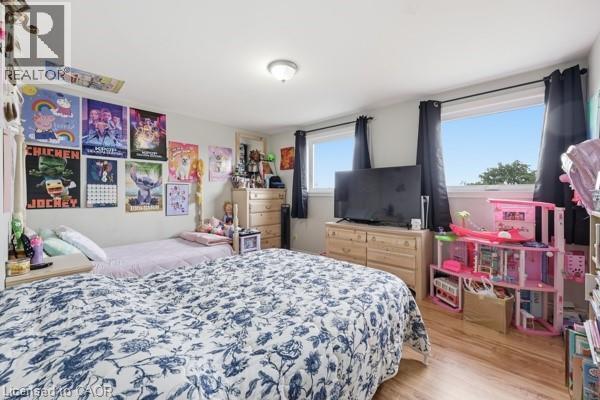 Room featuring wood-finish flooring, two windows with dark curtains, and a flush-mount ceiling light - 16 Harrison Avenue, Hamilton, ON