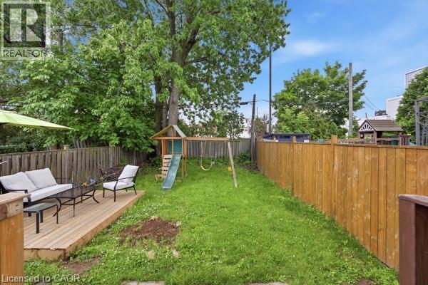 Expansive backyard featuring a natural wood deck, mature trees, and a wooden privacy fence - 16 Harrison Avenue, Hamilton, ON