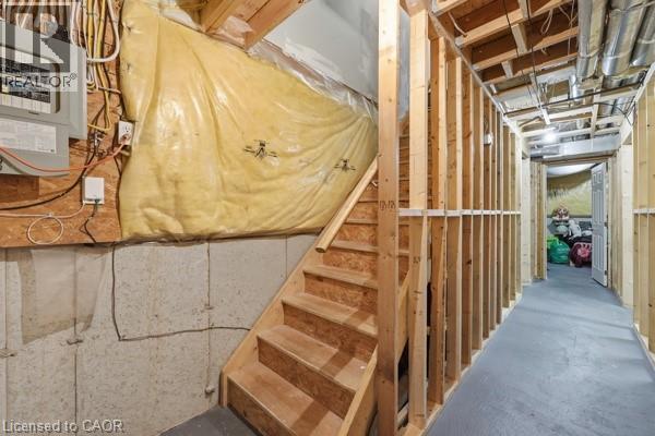 Unfinished basement space featuring exposed wood framing, concrete foundation walls, a wood staircase, and visible utility infrastructure including electrical paneling and ductwork - 16 Harrison Avenue, Hamilton, ON