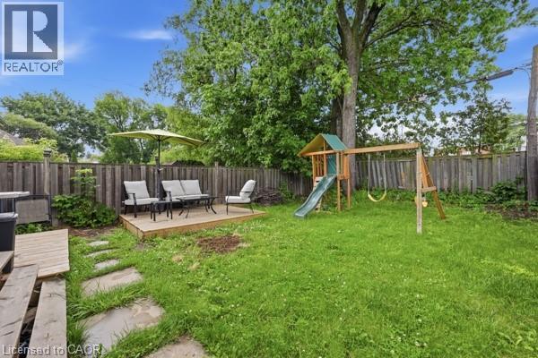 Expansive backyard featuring a wood deck patio, stone paver pathway, privacy fencing, and mature trees - 16 Harrison Avenue, Hamilton, ON
