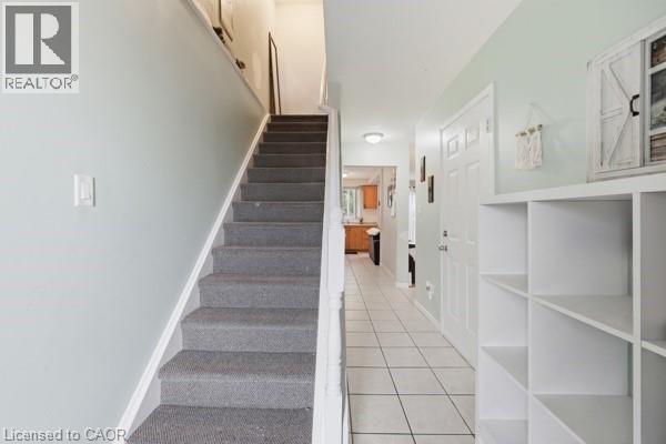 Carpeted staircase with white risers and handrail, alongside a tiled entryway - 16 Harrison Avenue, Hamilton, ON
