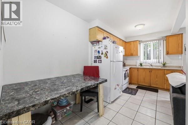 Kitchen featuring wood cabinetry, white appliances, and a window with blinds - 16 Harrison Avenue, Hamilton, ON