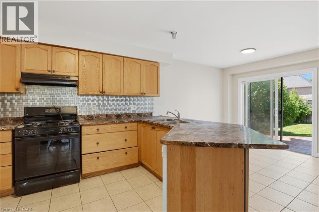 Kitchen featuring wood cabinetry, a mosaic tile backsplash, a black gas range, and a breakfast bar - 43 Decaro Crescent, Cambridge, ON