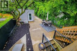 Concrete patio area featuring a detached structure with vinyl siding, mature trees, and landscaping with dark mulch -
