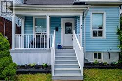 Blue siding exterior with a white-railed porch featuring a white entry door, gray steps, and white window trim -