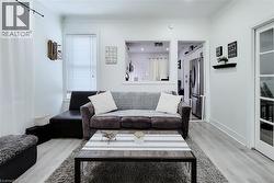Spacious living area featuring light wood-finish flooring, white walls, and a large window with blinds -