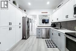 Modern kitchen featuring light wood-finish flooring, two-tone cabinetry with black hardware, stainless steel appliances, and a mosaic tile backsplash -