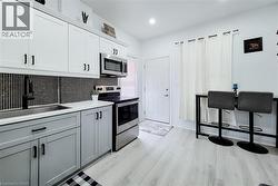 Kitchen featuring stainless steel appliances, mosaic tile backsplash, two-tone cabinetry, and wood-finish flooring -