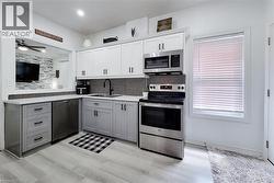 Kitchen featuring two-tone cabinetry with black hardware, stainless steel appliances, and wood-finish flooring -