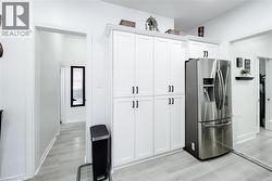 Full-height white cabinetry with black hardware, stainless steel refrigerator, light wood-finish flooring, white walls, and a mirrored closet door -