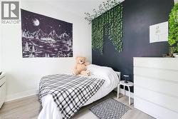 Bedroom featuring a dark accent wall with artificial hanging greenery, light wood-finish flooring, white baseboards, and white painted walls -