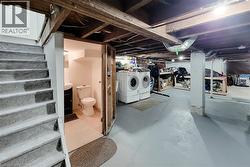 Basement utility space featuring a full staircase with carpeted treads, a dedicated laundry area with appliances, and a separate half-bathroom with a vanity sink and toilet -