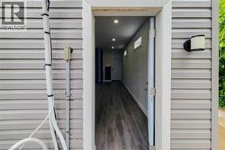 Siding exterior featuring a contemporary outdoor wall sconce and an open doorway revealing interior wood-finish flooring, recessed lighting, and transom windows -