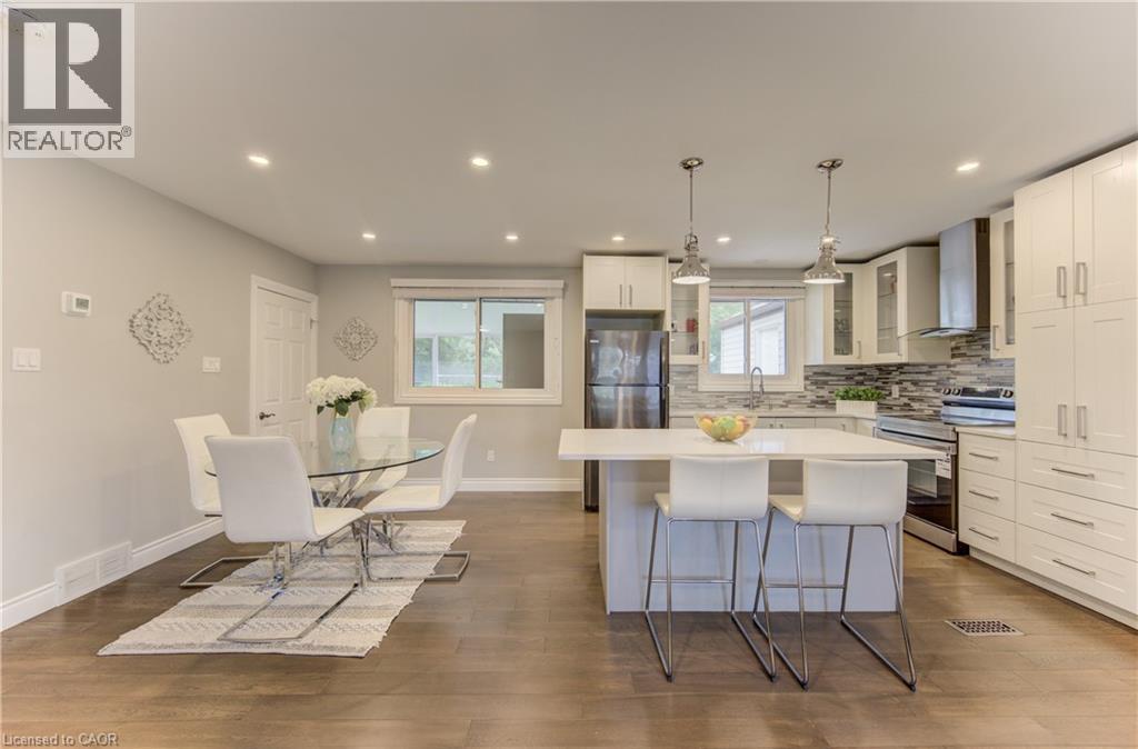 Open-concept kitchen and dining area featuring wood-finish flooring, recessed lighting, and a white kitchen island with seating - 619 Forest Hill Drive, Kitchener, ON