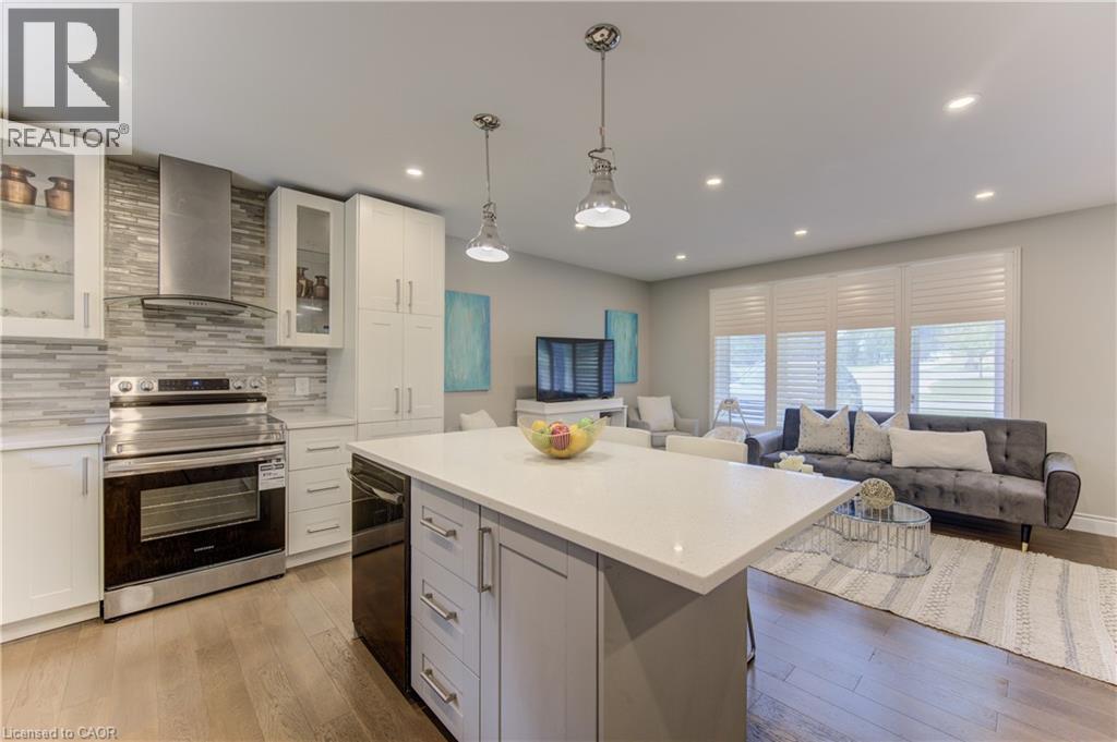 Open-concept living space featuring a kitchen with white cabinetry, stainless steel appliances, a tiled backsplash, and a central island with a solid surface countertop - 619 Forest Hill Drive, Kitchener, ON