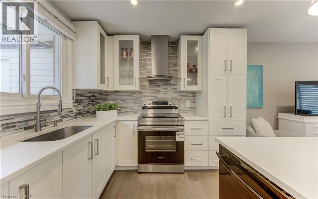 Modern kitchen featuring white cabinetry, a stainless steel range and hood, a mosaic tile backsplash, and light-tone countertops - 619 Forest Hill Drive, Kitchener, ON