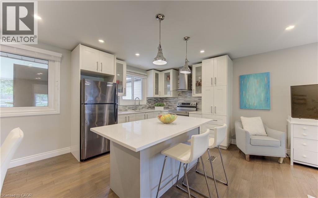 Open-concept kitchen featuring white shaker cabinetry, stainless steel appliances, a center island with a light-toned countertop, and recessed lighting - 619 Forest Hill Drive, Kitchener, ON