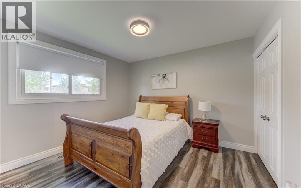 Bedroom featuring wood-finish flooring, a contemporary ceiling light fixture, a window with white trim, and a paneled white door - 619 Forest Hill Drive, Kitchener, ON
