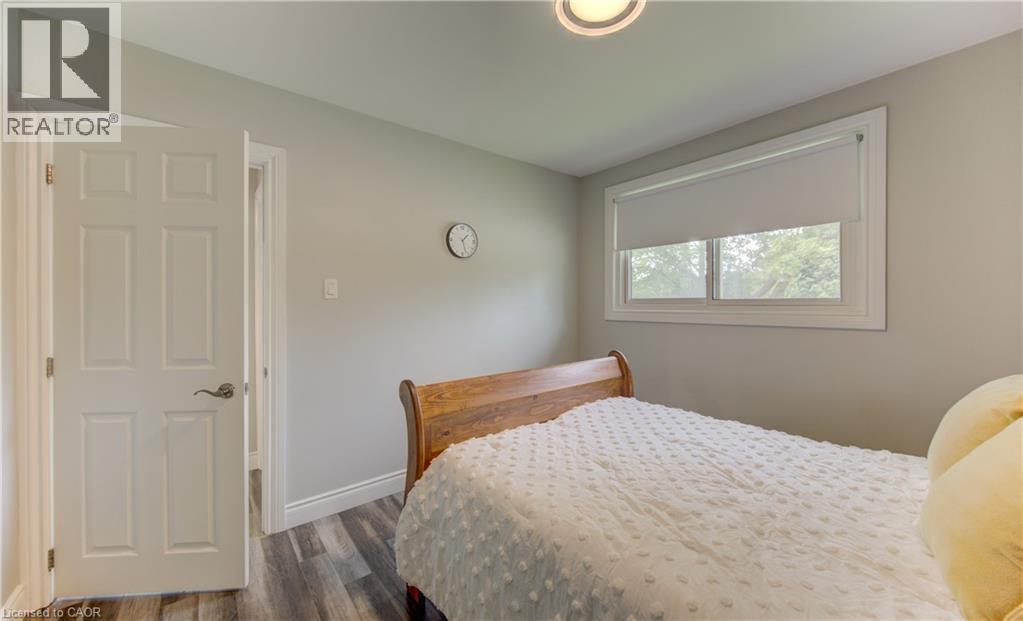 Bedroom featuring wood-finish flooring, a window with roller shade, and a six-panel interior door - 619 Forest Hill Drive, Kitchener, ON