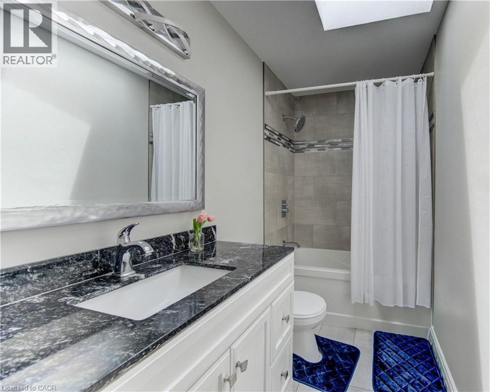 Bathroom featuring a dark speckled countertop vanity with an undermount sink, a framed mirror, and a tub with a tiled surround - 619 Forest Hill Drive, Kitchener, ON