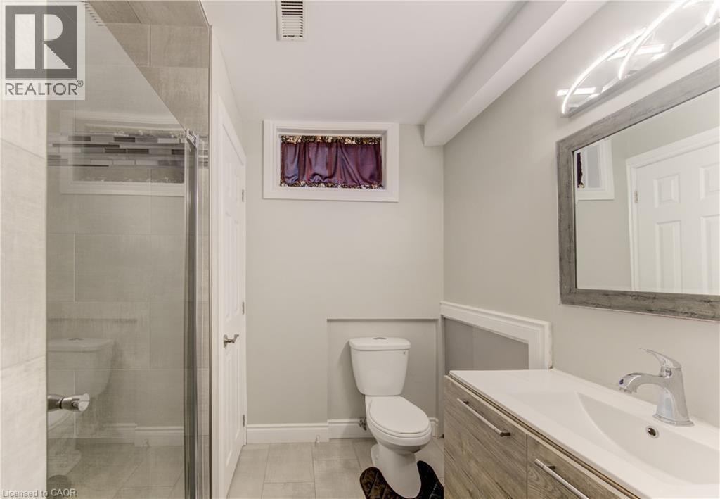 Contemporary bathroom featuring a glass-enclosed shower with tile surround and mosaic accent, a wood-finish vanity with an integrated sink, a framed mirror with modern lighting, and tile flooring - 619 Forest Hill Drive, Kitchener, ON