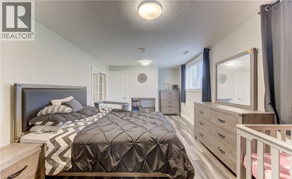 Spacious bedroom featuring wood-finish flooring, light neutral wall paint, a window with horizontal blinds, and a built-in overhead light fixture - 619 Forest Hill Drive, Kitchener, ON