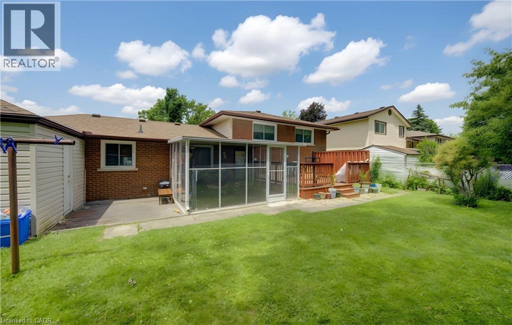 Rear exterior featuring a screened-in sunroom, multi-level wood deck, and a large grassy yard - 619 Forest Hill Drive, Kitchener, ON