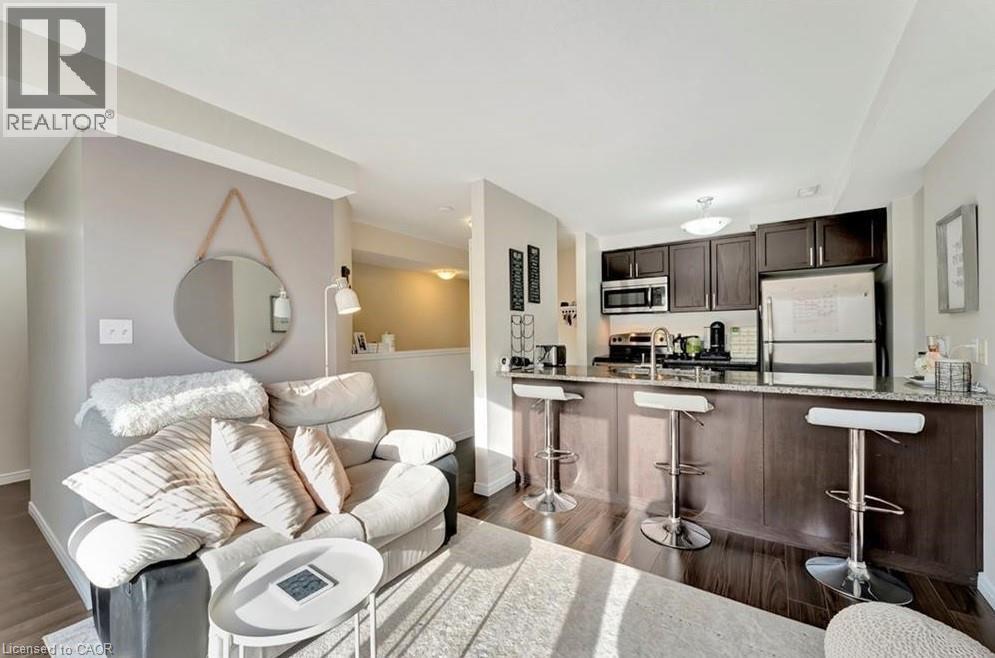 Open-concept living space featuring wood-finish flooring, a kitchen island with seating, dark wood cabinetry, and stainless steel appliances including a refrigerator and microwave - 236 Rachel Crescent Unit# E, Kitchener, ON