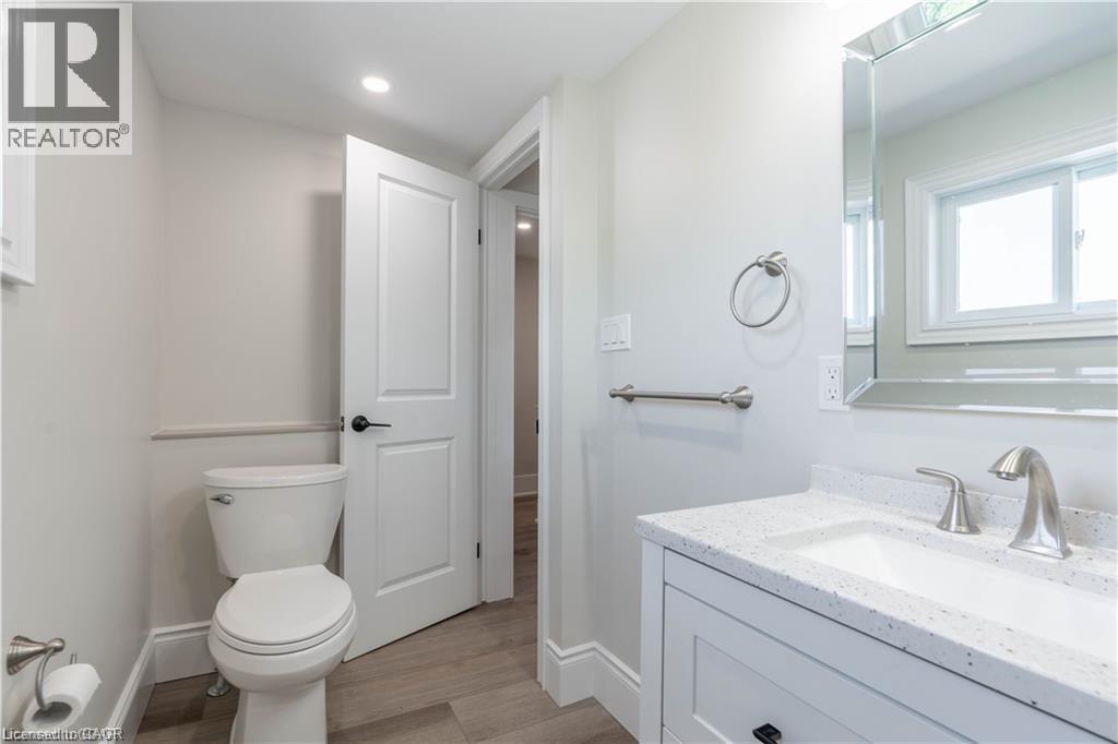 Bathroom featuring a modern vanity with a white countertop and integrated sink, a large mirrored medicine cabinet, brushed nickel fixtures, and wood-finish flooring - 66 Queen Street W, Cambridge, ON