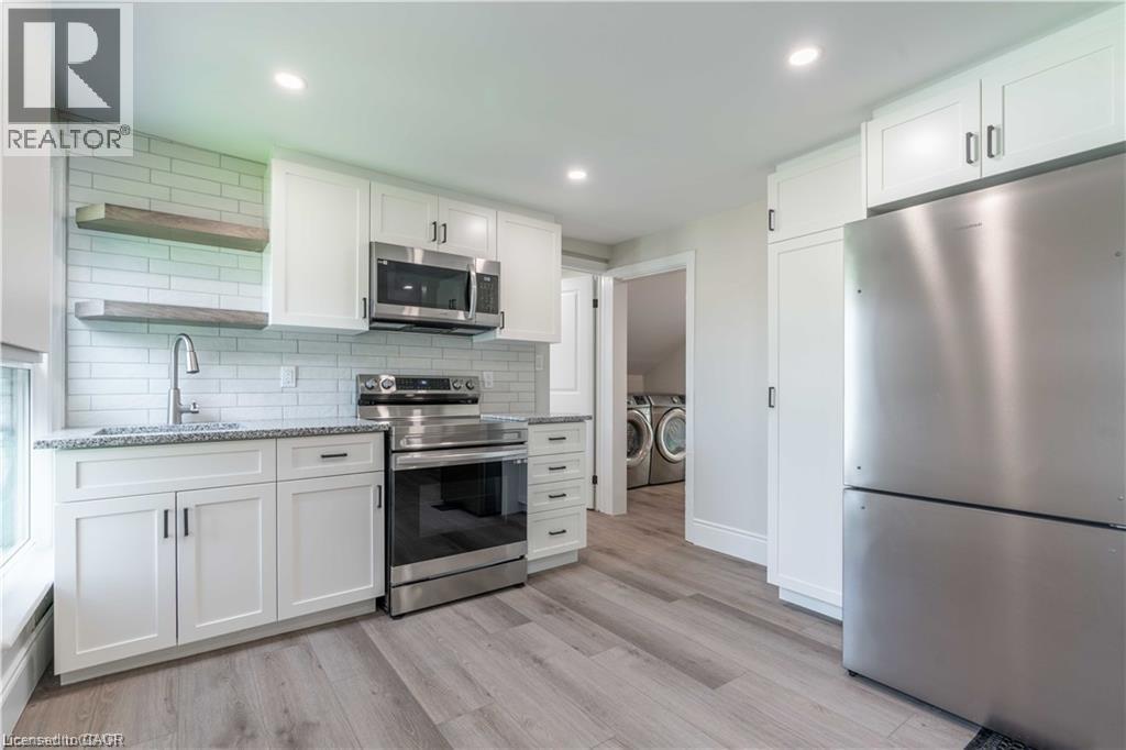 Modern kitchen featuring white shaker cabinetry, stainless steel appliances, granite countertops, and wood-finish flooring - 66 Queen Street W, Cambridge, ON