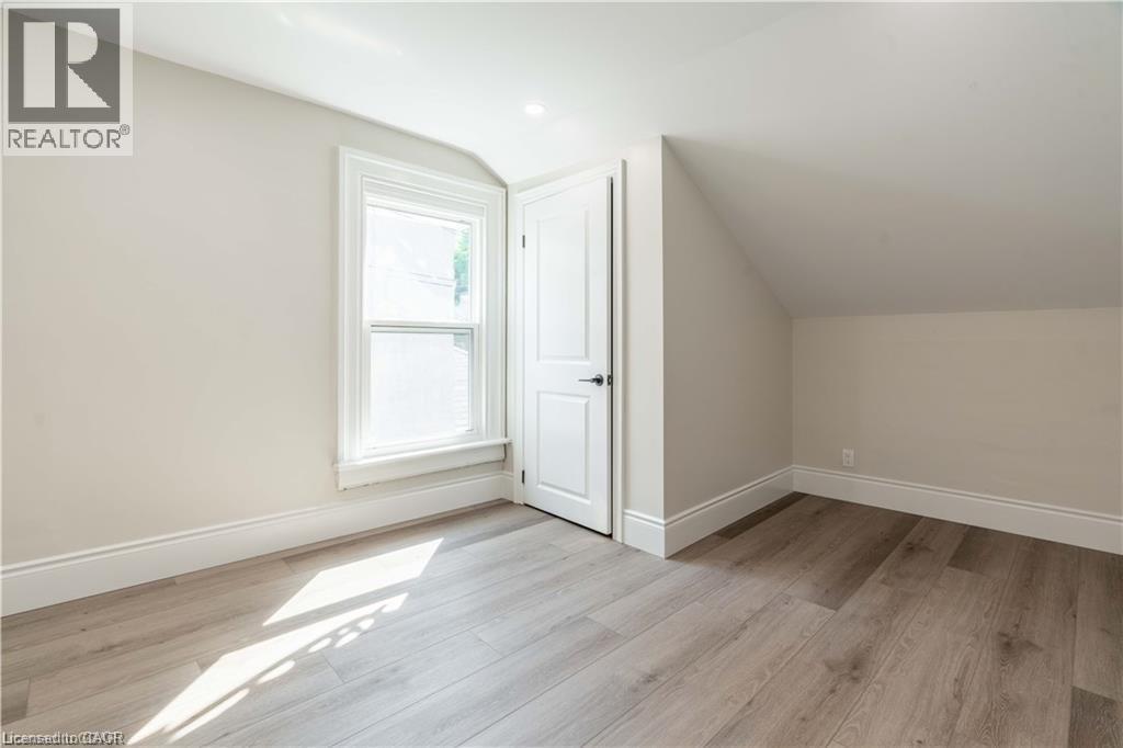 Room featuring light wood-finish flooring, white baseboards, a single window with white trim, a recessed ceiling light, and a white interior door with black hardware - 66 Queen Street W, Cambridge, ON
