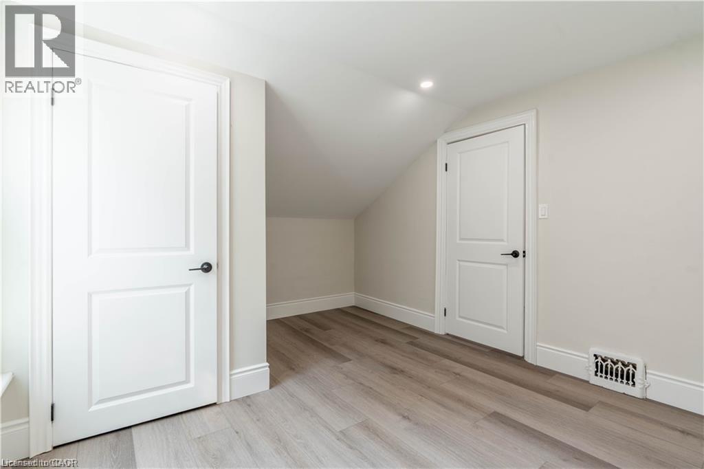 Attic space featuring wood-finish flooring, white paneled doors with matte black hardware, recessed lighting, and sloped ceilings - 66 Queen Street W, Cambridge, ON