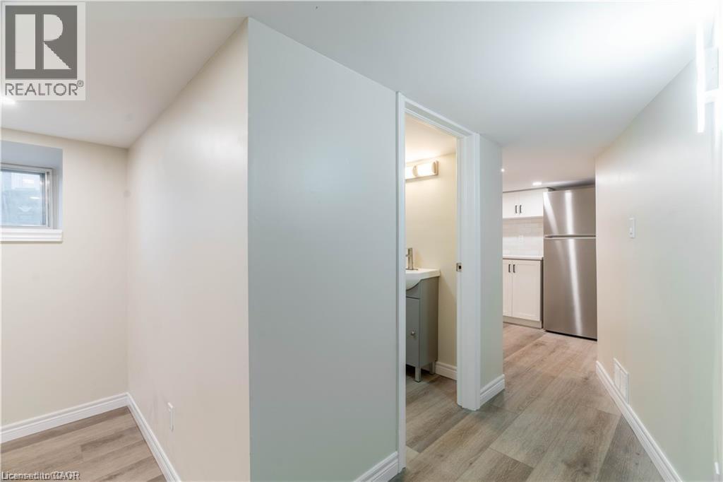 Wood-finish flooring throughout, with a window providing natural light, a compact kitchen area featuring stainless steel appliances, and a bathroom with a vanity and wall-mounted light fixture - 66 Queen Street W, Cambridge, ON
