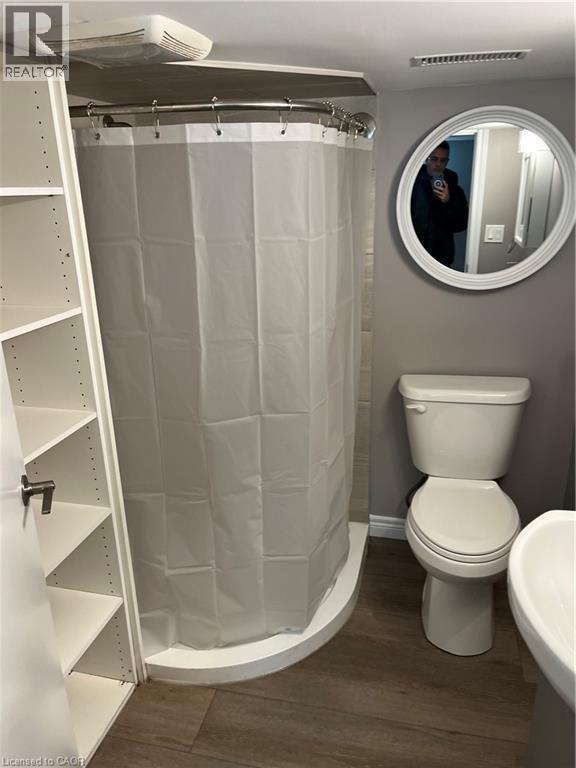 Bathroom featuring a corner shower with a curved curtain rod, a white toilet, and wood-finish flooring - 66 Queen Street W, Cambridge, ON