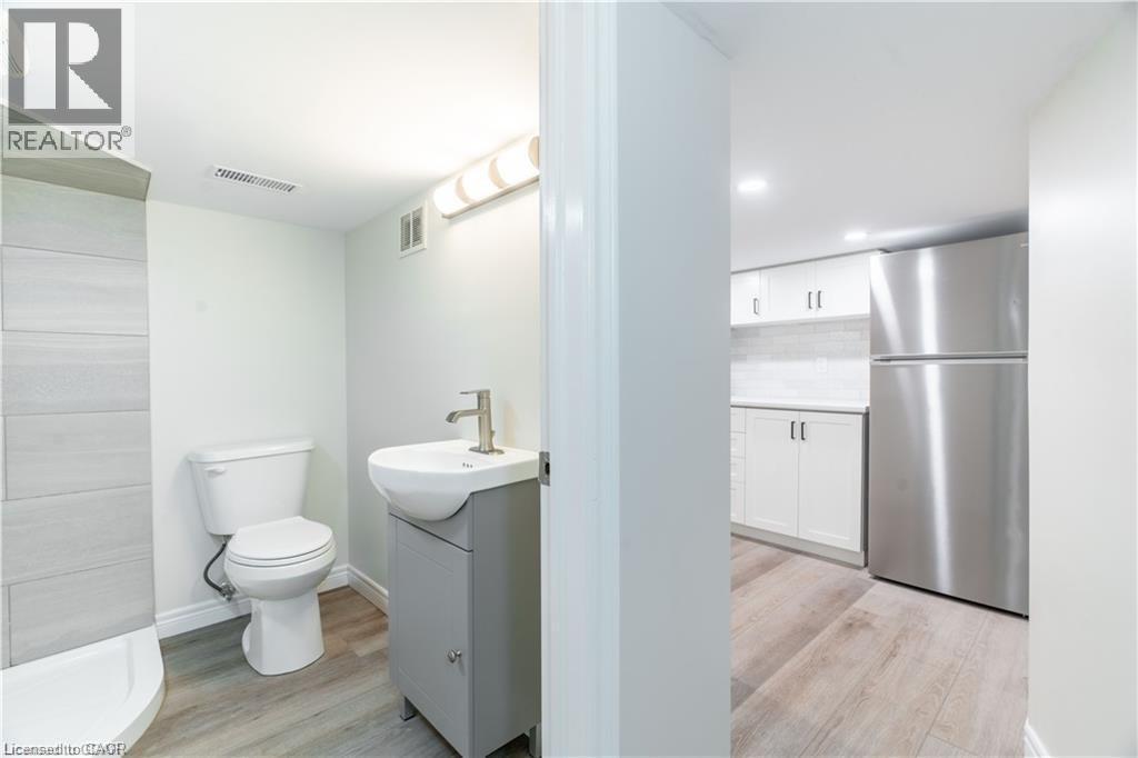 Bathroom featuring a white toilet, contemporary vanity with a white vessel sink, and an adjacent shower with horizontal tile detailing - 66 Queen Street W, Cambridge, ON