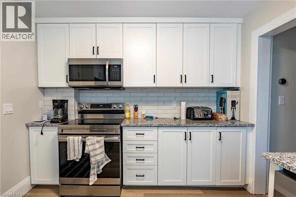 Kitchen featuring white shaker-style cabinetry with black hardware, a stainless steel range, and a coordinating built-in microwave - 66 Queen Street W, Cambridge, ON