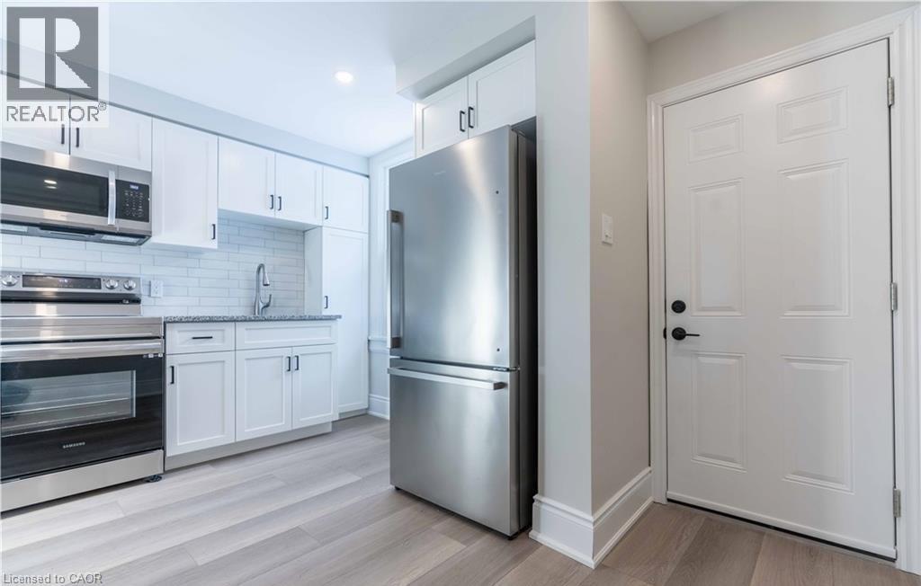 Modern kitchen featuring white shaker cabinetry, stainless steel appliances, a subway tile backsplash, and light wood-finish flooring - 66 Queen Street W, Cambridge, ON