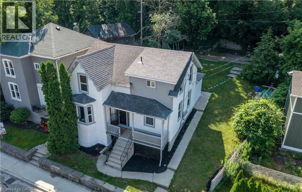 Two-story property featuring a front porch with railing, bay window, and a stone retaining wall - 66 Queen Street W, Cambridge, ON