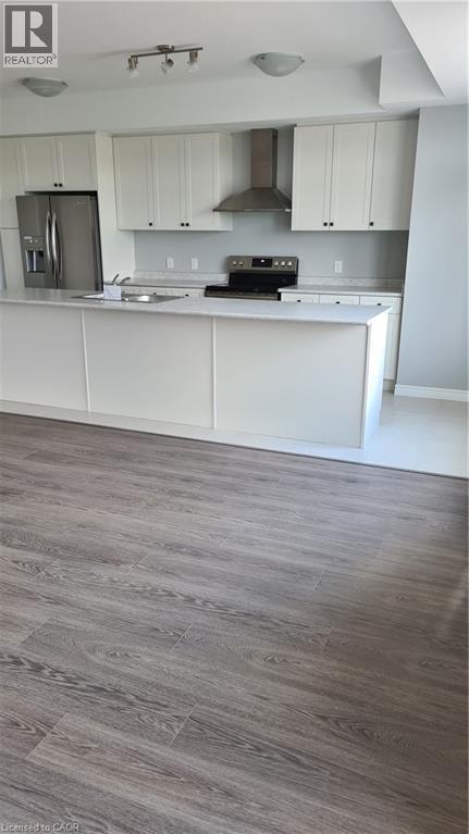 Modern kitchen featuring white cabinetry, stainless steel appliances, a center island with countertop, a tile backsplash, and wood-finish flooring - 42 Wheat Lane Unit# 42, Kitchener, ON
